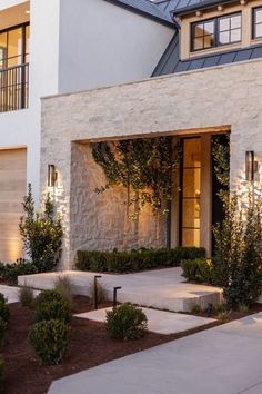 a modern house with stone facade and landscaping in front of the garage door at night