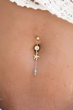 the back of a woman's stomach wearing a gold belly ring with an anchor and cross on it