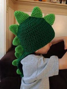 a little boy wearing a green crocheted dinosaur hat