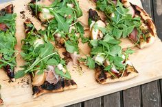 a wooden cutting board topped with slices of pizza covered in veggies and meat