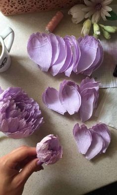 a person is making purple flowers out of crepe paper on a table next to a cup of coffee