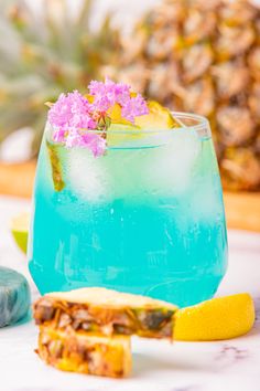 a blue drink with lemon wedges on the side and a pineapple in the background