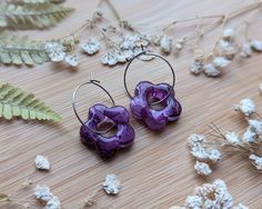 two purple flower shaped earrings sitting on top of a wooden table next to dried flowers