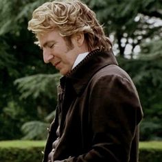 a man with blonde hair is looking down at his cell phone while standing in front of some trees