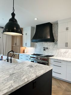 a kitchen with marble counter tops and black pendant lights over the stove top, along with white cabinets