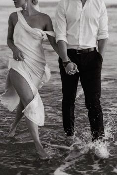 a man and woman are walking in the ocean water holding each other's hands