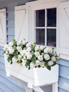 white roses are hanging from the side of a blue house with shutters and windows