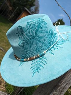 This truly one-of-a-kind hand burnt fedora is perfect to add a whimsical flare to your outfit or hang as a unique nature inspired wall decoration. It's burned entirely by hand using a pyrography tool with an original and entirely freehanded design (never using a stencil or laser machine.) The buttery soft mint faux suede material burns a gorgeous shade of turquoise. This charming design features a luna moth along the side of the hat's crown in front of snowdrop flowers and ferns. I adjusted the Unique Handmade Hat Bands For Beach, Handmade Adjustable Artistic Hat Bands, Unique Handmade Fedora For The Beach, Unique Handmade Fedora For Beach, Handmade Artistic Adjustable Hat Band, Adjustable Hand Painted Hat Bands For Beach, Handmade Adjustable Artistic Fedora, Adjustable Hand Painted Hat Bands For Festivals, Adjustable Hand Painted Fedora For Festivals