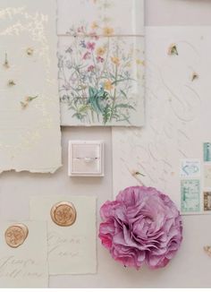 a pink flower sitting on top of a table next to some cards and envelopes