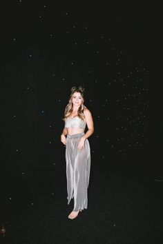 a woman standing in front of a black background wearing a silver skirt and crop top