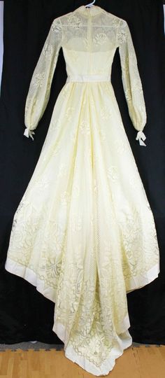 "Ivory dress, heavy-weight polyester lined with a cotton type of lace Grosgrain ribbon trim, sweetheart neckline under the lace. Ribbon around waist with long ribbon strands hanging from waist. Long sleeves with ribbon gathered cuffs. High neckline with dainty flower embroidered trim Train comes to a V like point On left-back arm seam, there is some lace stitching that has loose strands. Metal zipper closure No tags anywhere, appears to be handmade Woman's Size 6/8 based on measurements Approx m Cream Wedding Night Gown With Lace Trim, Ceremony Lace Dress With Sweetheart Neckline, Lace Dresses With Sweetheart Neckline For Ceremony, Lace Gown With Sweetheart Neckline For Ceremony, Sweetheart Neckline Lace Dress For Ceremonies, Lace Gown For Ceremony With Sweetheart Neckline, Cream Lace Dress With Lace Trim For Ceremony, Cream Lace Dress With Lace Bodice For Ceremony, Fitted Contrast Lace Dress For Wedding Night