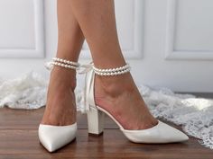 a woman's feet wearing white high heels with pearls on the ankle and heel