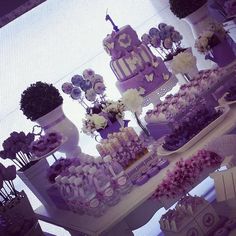 a table topped with lots of purple and white cake next to tall vases filled with flowers