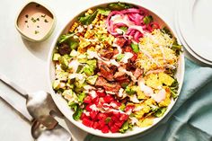 a large salad with meat, vegetables and dressing in a bowl next to a spoon