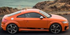 an orange car is parked on the side of the road by the water and hills