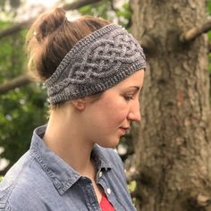 a woman wearing a knitted headband looking down at her cell phone while standing in front of a tree