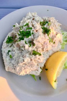 a white plate topped with crab salad next to a lemon wedge