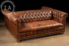 a brown leather couch sitting on top of a cement floor next to a black wall