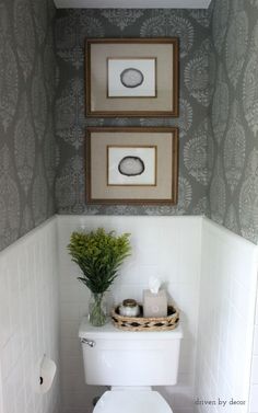 a white toilet sitting in a bathroom next to a wall with two pictures above it