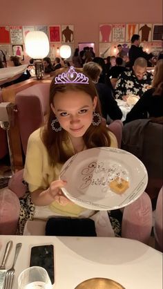 a girl in a tiara holding up a plate