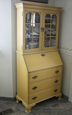 a yellow china cabinet with glass doors and drawers on the top, in front of a white wall