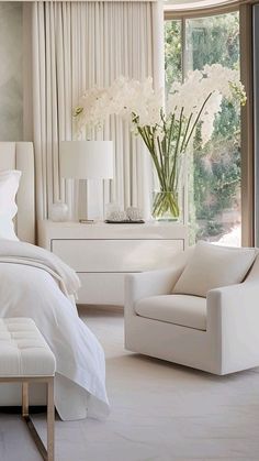 a bedroom with white furniture and flowers in vases on the nightstand next to the bed