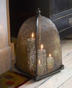 two lit candles are sitting in a metal lantern on the floor next to a fireplace