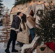 a man and woman kissing in front of a camper with christmas lights on it