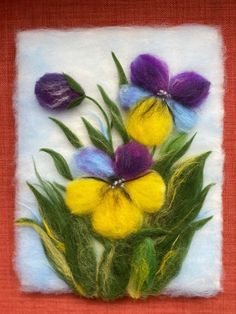 needled flowers are displayed on a piece of felted art work, with green leaves and purple pansies in the center