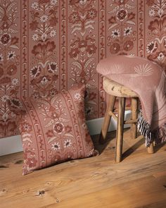 two pillows and a stool in front of a wallpapered room with wood flooring