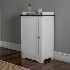 a white cabinet with a black top on the floor next to a wooden floor and gray walls