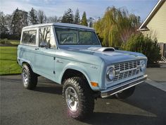 an old blue ford bronco is parked in front of a house