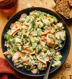 a blue bowl filled with salad next to crackers and a glass of beer on the side