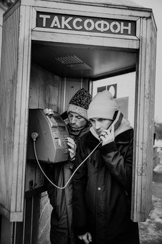 black and white photograph of two people talking on telephones in an old phone booth