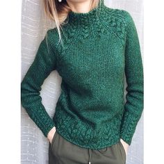 a woman is wearing a green sweater and standing in front of a white wall with her hands on her hips