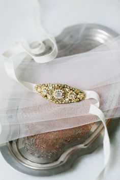 a white and gold wedding garter on top of a silver plate with a ribbon around it