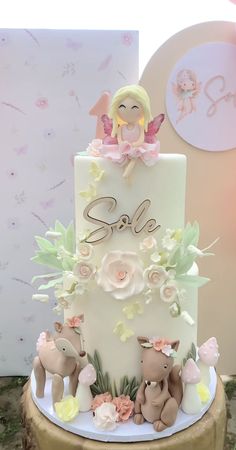 there is a white cake with pink flowers on it and a fairy figurine sitting on top