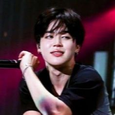 a young man sitting on top of a stage with a microphone in his hand and wearing a black shirt