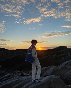 a man standing on top of a rock covered hillside at sunset with the sun setting behind him