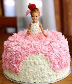 a pink and white cake with a doll sitting on top of the frosted cake