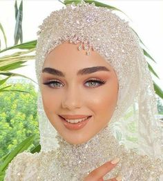 a woman wearing a white veil and diamond headdress smiles at the camera with her hand on her chest