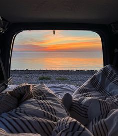 the view from inside an rv looking out onto the ocean at sunset with blankets and pillows on the bed