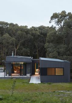 a house made out of shipping containers in the middle of a field with trees behind it