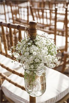 a mason jar filled with white flowers sitting on top of a wooden chair