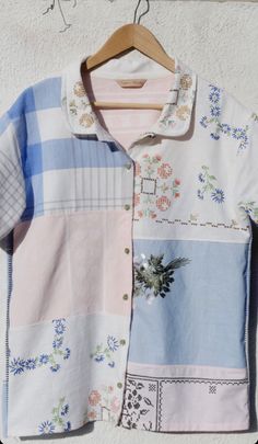 a shirt hanging up on a clothes hanger next to a white wall with blue and pink flowers