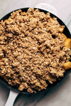 a skillet filled with granola on top of a marble counter next to a spoon