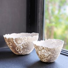 two white lace bowls sitting on top of a window sill