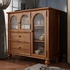 a wooden cabinet with glass doors in front of a window and rug on the floor