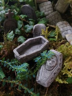 two stone statues sitting in the grass next to some plants and rocks with moss growing on them