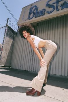 a woman leaning against the side of a building with her hands on her hips while wearing high heels